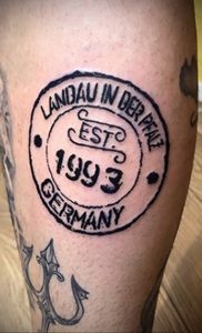 Фото тату с изображением винтажной печати на руке. Печать содержит надпись 'LANDAU IN DER PFALZ EST. 1993 GERMANY'.