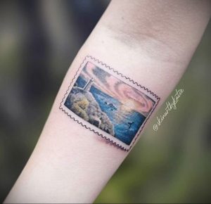 Фото тату на руке, изображающее морской пейзаж в рамке почтовой марки. Пастельные тона и детализированный рисунок татуировки.