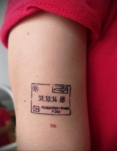 Фото тату на предплечье, имитирующее старый авиабилет с датой и названием аэропорта. Черно-белый рисунок татуировки в минималистичном стиле.
