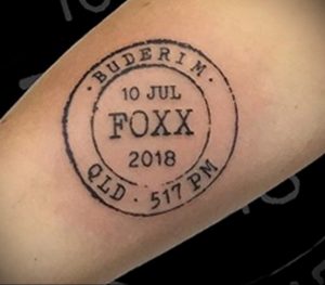 Фото тату: небольшая татуировка в виде почтового штемпеля с надписью 'BUDERIM 10 JUL FOXX 2018 QLD 517 PM' на руке.