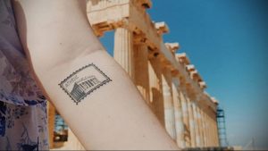 Фото тату на руке: минималистичная татуировка в виде почтовой марки с изображением Акрополя в Афинах и надписью "ATHENS".