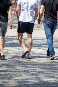 Фото тату на икре мужчины, идущего по улице. Видна часть татуировки в темных тонах, выполненной в реалистичном стиле.