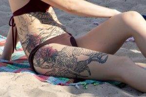 Крупный план татуировки на боку девушки, изображающей дракона, обвивающегося вокруг ярких красных цветов. Детализированный рисунок татуировки.