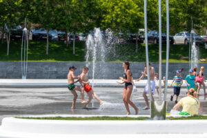Фотография детей, играющих в фонтане в солнечный день. Брызги воды, смех и радость на лицах. Идеальное изображение для летних идей тату.