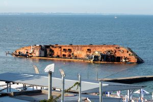 Фотография ржавого затонувшего корабля в море, голубое небо, спокойная вода. Подходит для эскиза тату в морской тематике или как символ стойкости.