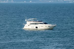 Фотография белой моторной яхты, плывущей по спокойному синему морю. Яхта современная, с белым корпусом и темным верхом.