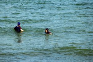 Фотография двух женщин, плавающих в море, одна смотрит в сторону, другая повернулась лицом к зрителю.