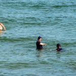 Фотография трех человек, плавающих в море: две женщины и мужчина, на фоне спокойной воды.