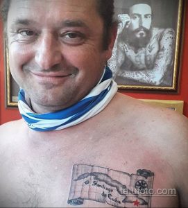 Фото тату на груди: реалистичный рисунок свитка с надписью "Santiago de Cuba", выполненный в черно-белых тонах.