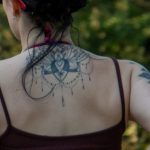 Фото тату на спине девушки: сложная мандала с множеством деталей и геометрических узоров. Черно-белый рисунок татуировки.