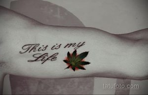 Фото тату надписи 'This is my Life' выполненной каллиграфическим шрифтом, рядом с реалистичным изображением листа каннабиса на руке.