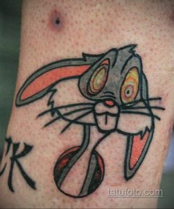 Цветная татуировка на руке, изображающая мультяшного персонажа Bugs Bunny. Олдскульный стиль, яркие цвета, четкие контуры.