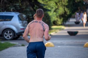 Фотография бегущего мужчины с татуировкой на спине. Надпись на латыни выполнена элегантным шрифтом, подчеркивая его атлетическое телосложение и индивидуальность.