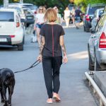 Фото тату на руке: женщина гуляет с собакой, на руке виден реалистичный рукав с портретом и цветами, выполненный в черно-серых тонах.