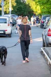 Фото тату на руке: женщина гуляет с собакой, на руке виден реалистичный рукав с портретом и цветами, выполненный в черно-серых тонах.
