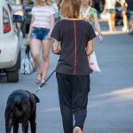 Фото тату на руке: женщина гуляет с собакой, на руке виден реалистичный рукав с портретом и цветами, выполненный в черно-серых тонах.