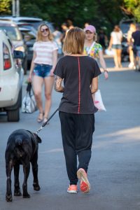 Фото тату на руке: женщина гуляет с собакой, на руке виден реалистичный рукав с портретом и цветами, выполненный в черно-серых тонах.