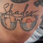 Татуировка на руке с изображением солнцезащитных очков и надписью 'Shades'. Стильный и лаконичный дизайн.