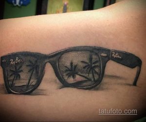Фото тату на руке: реалистичное изображение очков Ray-Ban, в линзах которых отражаются пальмы. Стильный и детализированный рисунок.