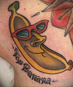 Фото тату на руке: банан в солнцезащитных очках с надписью "Top Banana", выполненный в ярких желтых и красных тонах. Оригинальный и забавный рисунок татуировки.