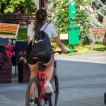 Фотография девушки, едущей на велосипеде по городу. На ее спине видна небольшая татуировка в виде пчелы.