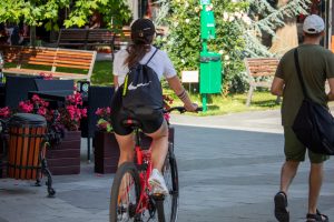 Фотография девушки, едущей на велосипеде по городу. На ее спине видна небольшая татуировка в виде пчелы.