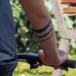 Крупный план руки велосипедиста с татуировкой из трех горизонтальных черных линий на предплечье. Минималистичный дизайн.