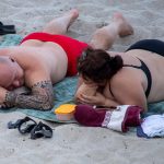 Фотография пары, отдыхающей на пляже. У мужчины на предплечье видна татуировка в полинезийском стиле, выполненная в черных тонах.