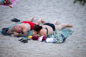Фотография пары, отдыхающей на пляже. У мужчины на руке видна масштабная татуировка в стиле полинезийский орнамент, покрывающая плечо и предплечье.