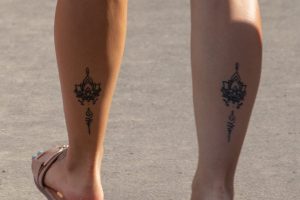Фотография двух женских лодыжек с идентичными татуировками: цветок лотоса и символ Ом, выполненные в черном цвете. Идеально для подруг или пар.