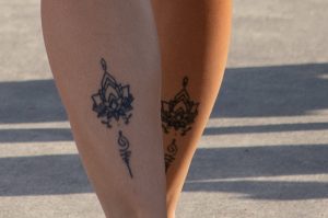 Фотография двух женских лодыжек с изящными татуировками: цветок лотоса и символ Ом, выполненные в черном цвете. Идеально для любителей минимализма.