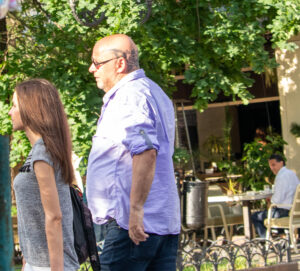 Фото татуировки: черно-серая татуировка с изображением розы и ветвей, расположенная на затылке мужчины. Мужчина в рубашке, вид сбоку.