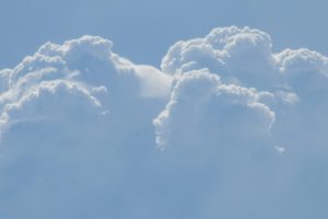 Фотография голубого неба с большими, пышными кучевыми облаками. Облака имеют ярко-белый цвет и сложную структуру.