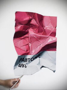 Фотография листа бумаги с номером цвета Pantone 493, смятого и зафиксированного рукой. Идеально для вдохновения и создания эскизов тату.
