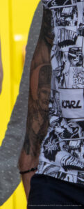 Фото тату: реалистичный портрет Карла Лагерфельда на руке мужчины. Татуировка выполнена в черно-белой гамме и отличается высокой детализацией.