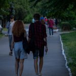 Фотография пары, идущей по парку. У мужчины на руке видна татуировка змеи, обвивающей предплечье. Снимок сделан в солнечный день.