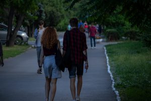 Фотография пары, идущей по парку. У мужчины на руке видна татуировка змеи, обвивающей предплечье. Снимок сделан в солнечный день.