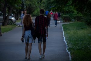 Фотография пары, идущей по парку. У мужчины на руке видна татуировка змеи, обвивающей предплечье. Снимок сделан в солнечный день.