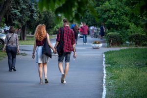 Фотография пары, идущей по парку. У мужчины на руке видна татуировка змеи, обвивающей предплечье. Снимок сделан в солнечный день.