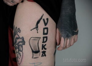 Фото татуировки на бедре с надписью 'VODKA' вертикально и изображением опрокинутого стакана. Черно-белый рисунок, простой стиль.