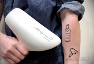 Фото минималистичной татуировки на руке с изображением бутылки Absolute Vodka и стакана. Тонкие черные линии, простой дизайн, современный стиль.