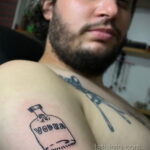 Фото тату на плече: черно-белое изображение бутылки водки с надписью VODKA. Минималистичный рисунок татуировки.