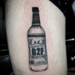 Фото тату на ноге: черно-белое изображение бутылки Mr. Boston с надписью B2F. Минималистичный рисунок татуировки в стиле дотворк.