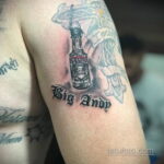 Фото тату бутылки Smirnoff Vodka на руке, выполненное в черно-серых тонах с надписью 'Big Andy' под ней.