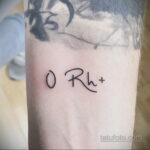 Фото минималистичной татуировки на руке с надписью 'O Rh+'. Тонкие черные линии, простой дизайн, символическое значение.