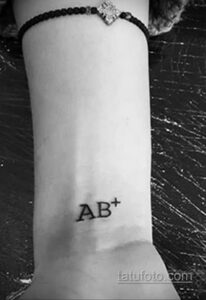 Простая татуировка с обозначением группы крови 'AB+'. Черно-белый минималистичный рисунок на запястье.