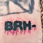 Фотография татуировки с указанием группы крови 'BRH-' на запястье, выполненной черными буквами с красными брызгами, имитирующими кровь.