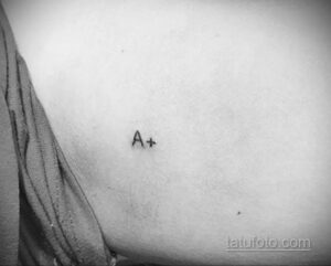 Фотография минималистичной татуировки с указанием группы крови 'A+' на ключице, выполненной тонкими черными линиями.