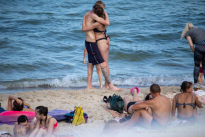 Фото тату на ноге парня, обнимающего девушку на пляже. Видна часть татуировки в виде темных узоров на коже.