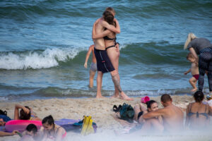 Фото тату на ноге парня, обнимающего девушку на пляже. Видна часть татуировки в виде темных узоров на коже.